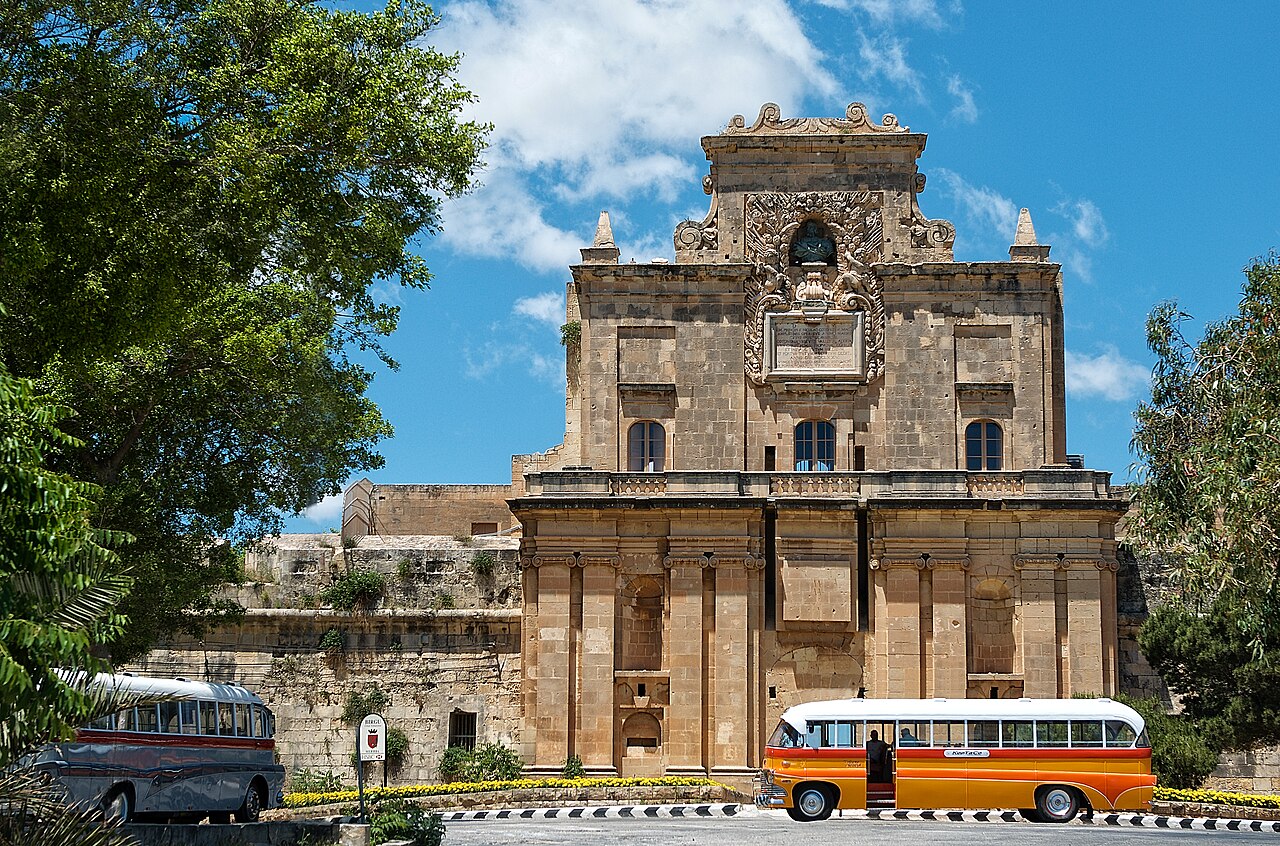 The Notre Dame Gate In Birgu With Old Traditional Maltese Bus In Front It
