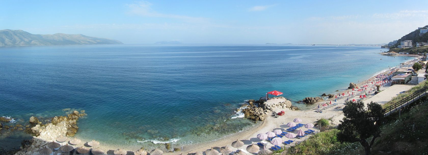 A panoramic view of the Vlora coastline with a mix of developed beaches and rugged cliffs.